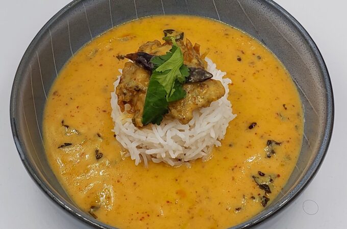 A bowl of Punjabi kadhi served with white rice, garnished with fresh coriander leaves.