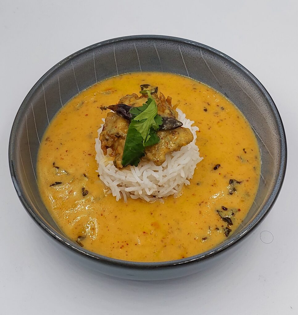 A bowl of Punjabi kadhi served with white rice, garnished with fresh coriander leaves.