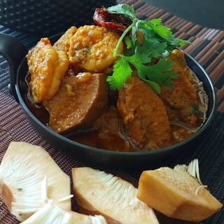 A bowl of authentic Bengali Echor Chingri, showcasing tender jackfruit and prawns in a rich, spicy curry, garnished with fresh coriander leaves.