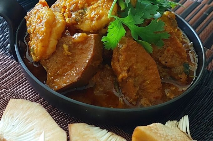 A bowl of authentic Bengali Echor Chingri, showcasing tender jackfruit and prawns in a rich, spicy curry, garnished with fresh coriander leaves.