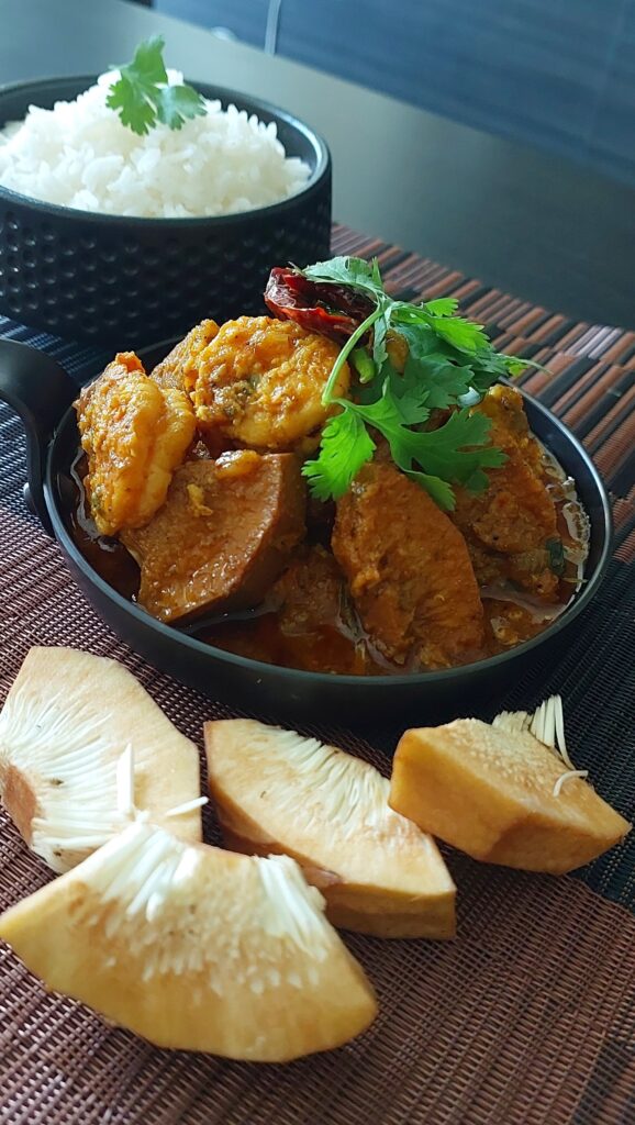 A bowl of authentic Bengali Echor Chingri, showcasing tender jackfruit and prawns in a rich, spicy curry, garnished with fresh coriander leaves.