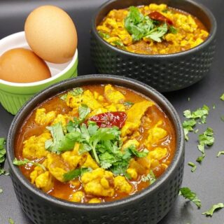 A bowl of Egg Bhurji Curry garnished with fresh coriander leaves, showcasing a vibrant yellow and red color with chunks of scrambled eggs in a rich tomato gravy.