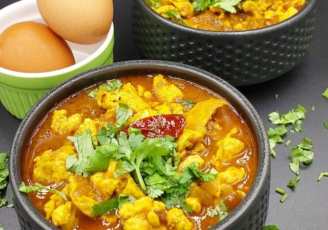 A bowl of Egg Bhurji Curry garnished with fresh coriander leaves, showcasing a vibrant yellow and red color with chunks of scrambled eggs in a rich tomato gravy.