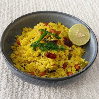 Lemon rice served in a bowl garnished with curry leaves, green chilies, lemon and peanuts.