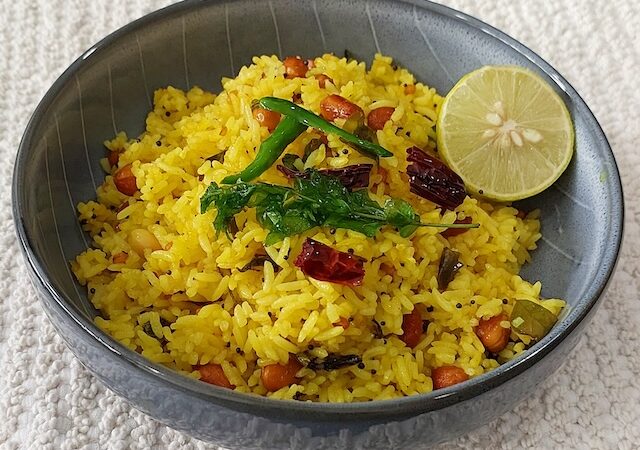 Lemon rice served in a bowl garnished with curry leaves, green chilies, lemon and peanuts.