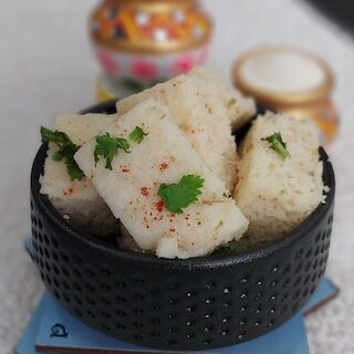 A bowl of soft and fluffy suji dhokla garnished with coriander leaves and served with green chutney.