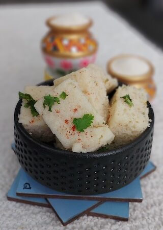 A bowl of soft and fluffy suji dhokla garnished with coriander leaves and served with green chutney.