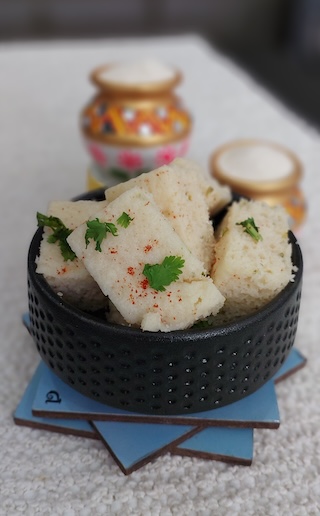 A bowl of soft and fluffy suji dhokla garnished with coriander leaves and served with green chutney.